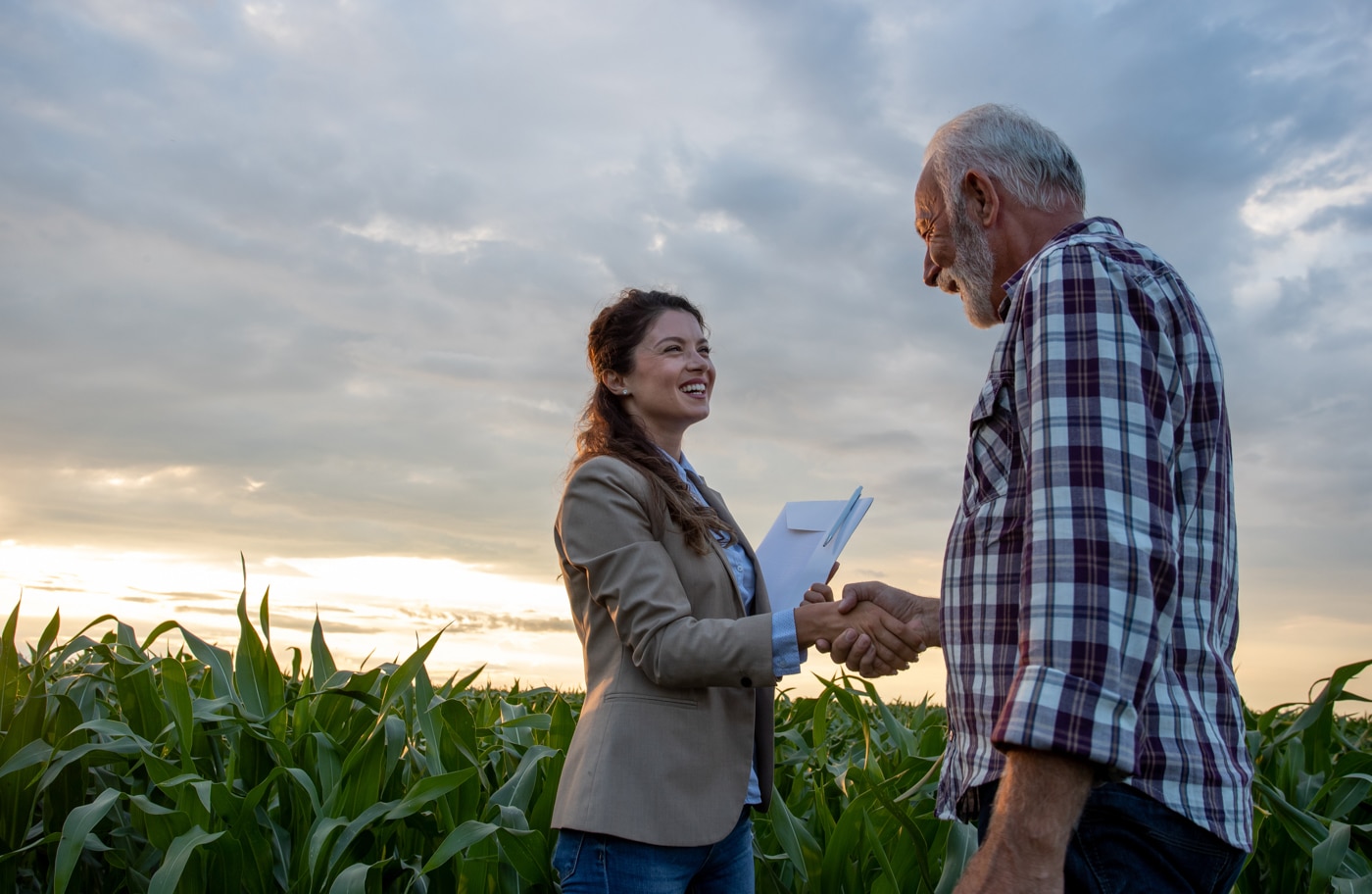 A landowner shaking hands with a buyer at the edge of a field